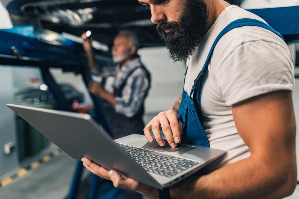Mécanicien automobile en combinaison orange utilisant un ordinateur portable pour diagnostic véhicule